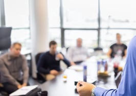 A photo of a businessman giving a presentation to a room full of colleagues.