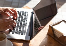 Hands typing on a laptop keyboard next to a cup of coffee