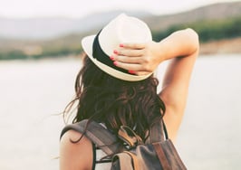 A millennial woman with her hand on a hat looking over a lake