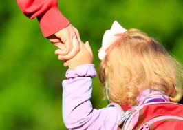 A mother holding a child's hand who is wearing a backpack