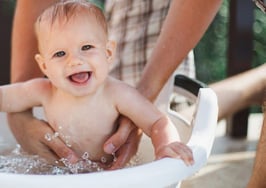 A baby being bathed in a basket outside