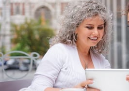 A mother and daughter sitting at a table together, looking at a tablet computer