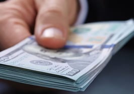 A man handing a stack of $100 bills to an unseen person