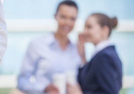 A man and woman whispering about a third person in the foreground