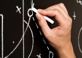 A hand outlining a game plan on a chalkboard