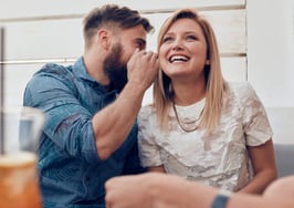 A young man whispers into a woman's ear