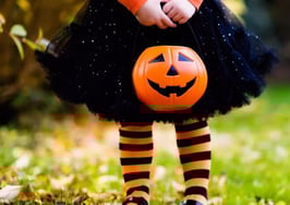 A young girl in a witch outfit with a Halloween candy pail
