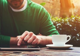 A young man working on a tablet with a smartphone and cup of coffee next to him