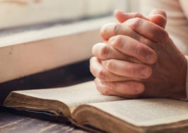 A woman's hands folded on a Bible