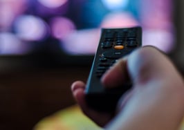 A hand holding a remote control pointed at a television