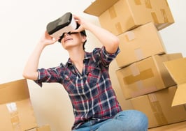 A woman looks through a virtual reality headset in the midst of boxes