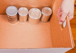 A pair of hands holding a box with cans