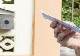 A man holding a letter by a mailbox