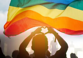 Pride community at a parade with hands raised and the LGBT flag.