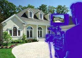 A silhouette of a person with a camera in front of a house to represent blockbuster listing videos.