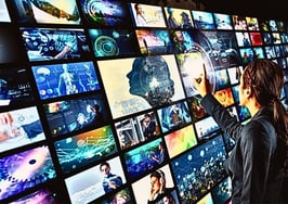 A woman standing in front of a wall of tv screens to illustrate how to multiply your output when you learn how to repurpose real estate content with AI.