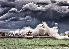 A tsunami hitting a marina and boat to symbolize real estate consolidation 2025.