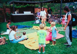 An image of a yard with blankets on the grass, parents with their toddlers to represent a baby rave open house.