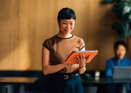 A confident woman using a digital tablet in a contemporary office environment. The setting conveys professionalism, technology, and productivity with a focus on modern work practices.