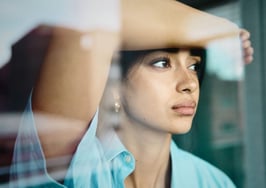 A person looks out a window, illustrating pent-up housing demand as prospective buyers wait for market conditions to improve.