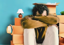 A man covering his face with moving boxes behind him to represent homebuyer's remorse.