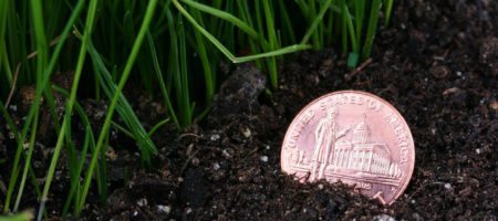 A penny laying on the ground, partly buried in soil.