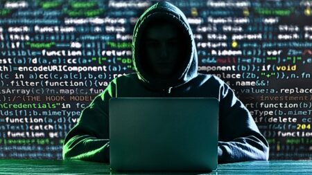 Man in hooded sweatshirt with no face in front of computer code to represent pig butchering financial scam