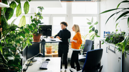 Two office colleagues looking at some work on a computer at a standing desk in a modern office space.