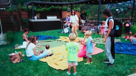 An image of a yard with blankets on the grass, parents with their toddlers to represent a baby rave open house.