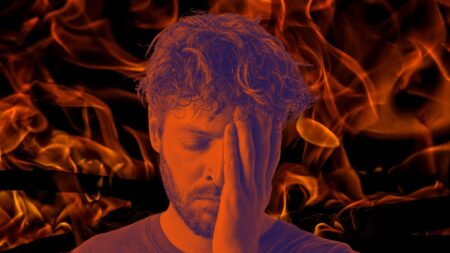 A picture of a man with his hand on his face who looks stressed in front of a firey background to represent listing agent burnout.
