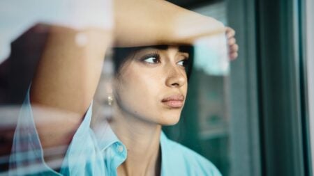 A person looks out a window, illustrating pent-up housing demand as prospective buyers wait for market conditions to improve.