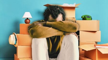 A man covering his face with moving boxes behind him to represent homebuyer's remorse.