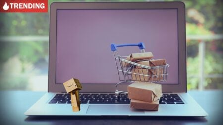 A small figure made of Amazon boxes looks at a computer behind a shopping cart full of packages, illustrating real estate data privacy.
